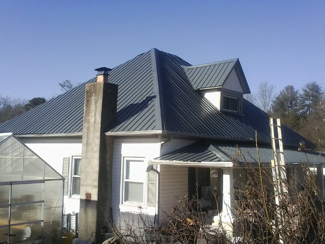 Dark blue standing seam metal roof on a white farmhouse with dormer — Slate & Tile Roof Repair by Roofing Brothers in Wendover