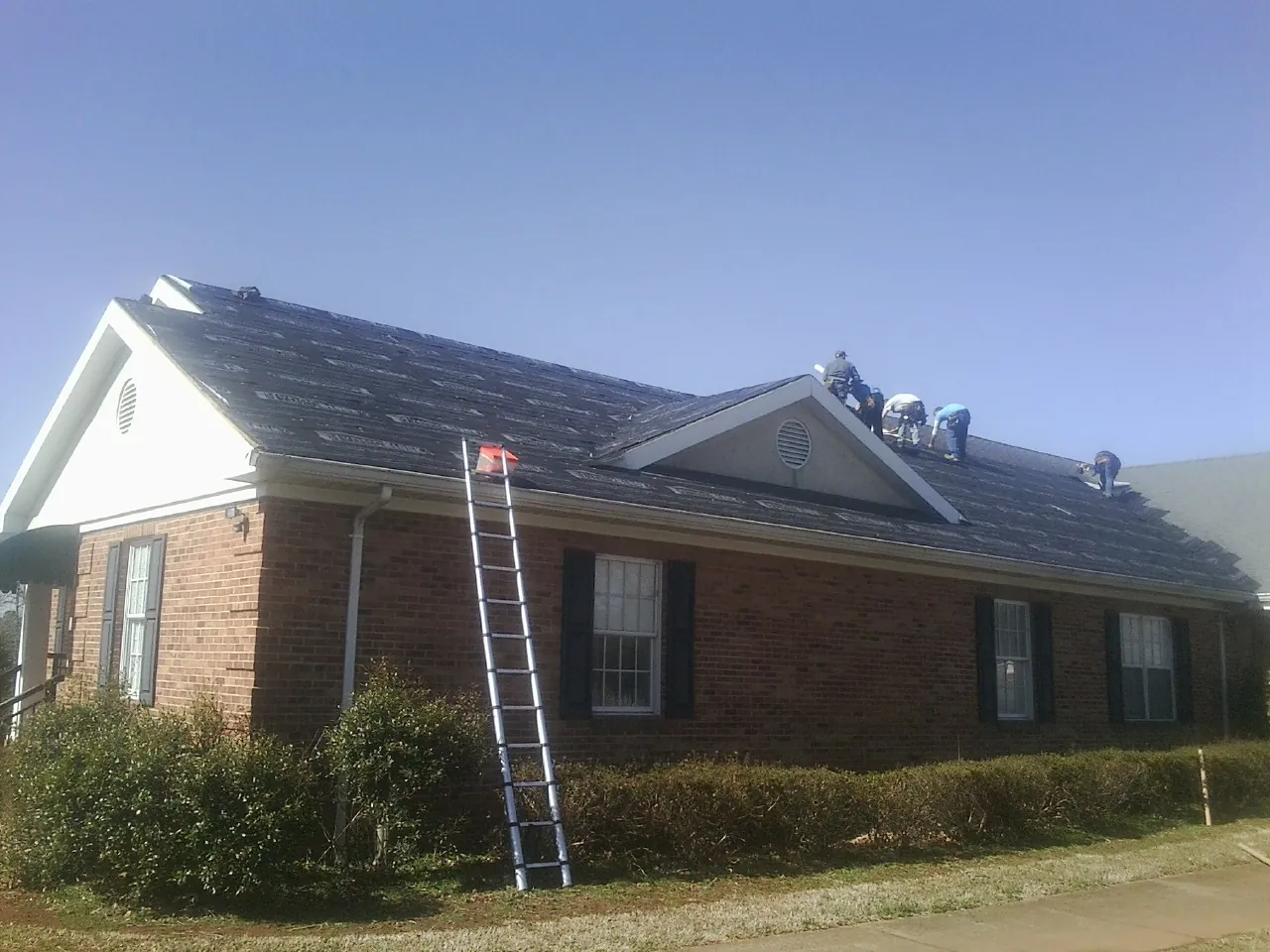 Crew tearing shingles off a brick ranch roof with a ladder set — Metal Roof Repair work by our crew in Wendover