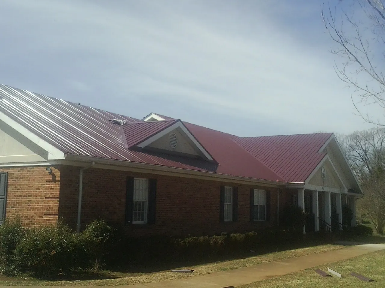 Red metal roof with gabled entries on a long brick building, from a Hail Damage Roof Repair job in Wendover