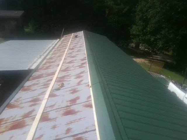 Old rusted panels beside newly installed green metal roofing — Wind Damage Roof Repair by Roofing Brothers in Wendover
