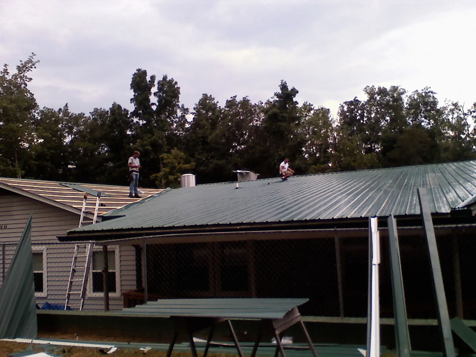 Two roofers installing green metal panels above a covered porch in Wendover