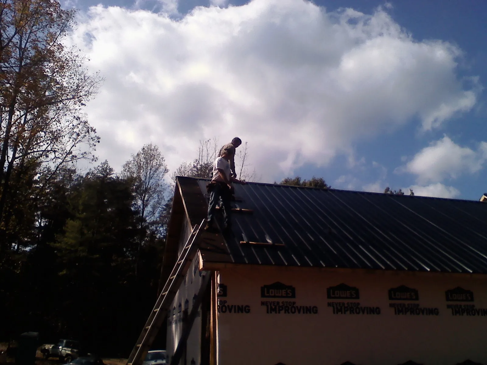 Roofer fastening dark metal panels high against a cloudy sky, from a Roof Inspection job in Wendover